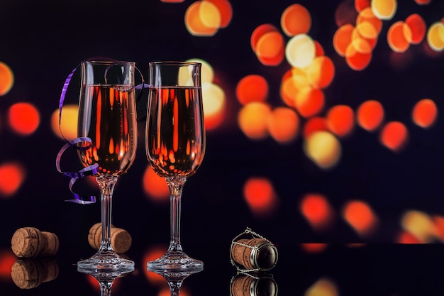 Due bicchieri di champagne rosa e decorazioni di Natale o Capodanno con un bokeh di luce dorata sul nero