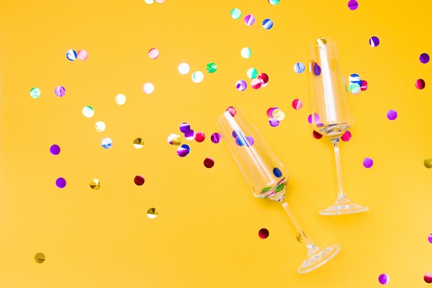 Due bicchieri di champagne su uno sfondo giallo cosparso di coriandoli, cerchi lucidi nel posto della copia dei bicchieri