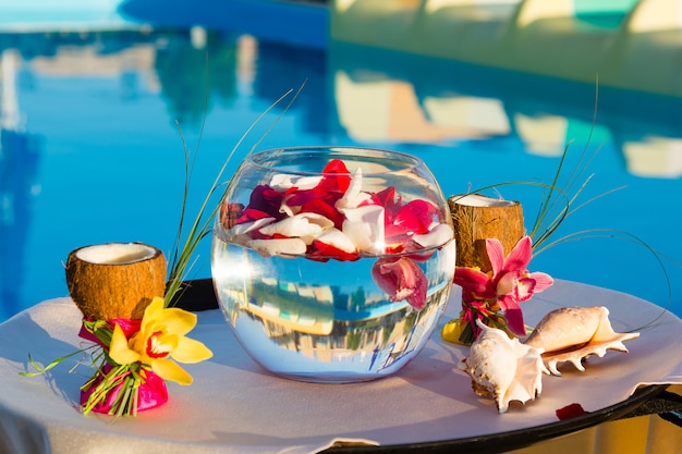 Due bicchieri di cocco con orchidee, due conchiglie e petali di rosa in un acquario