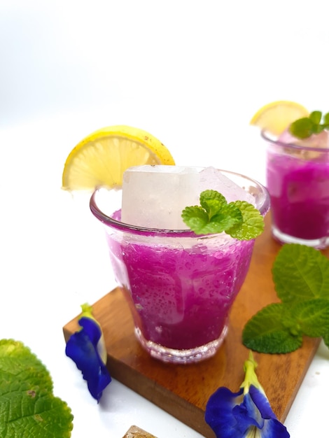Due bicchieri di cocktail viola con uno spicchio di lime e foglie di menta su una tavola di legno.