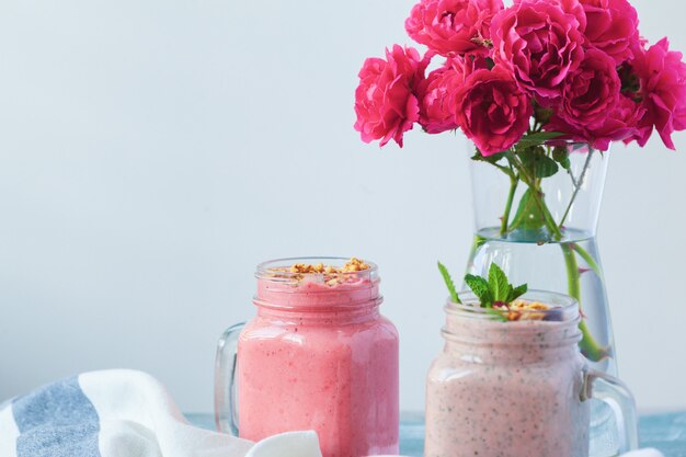 Due bicchieri di frullato sano con menta fresca sul vecchio tavolo rustico in legno con fiori di rosa freschi