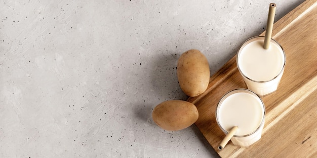 Due bicchieri di latte di patate vegano su tavola di legno su cemento Banner Vista dall'alto Spazio di copia