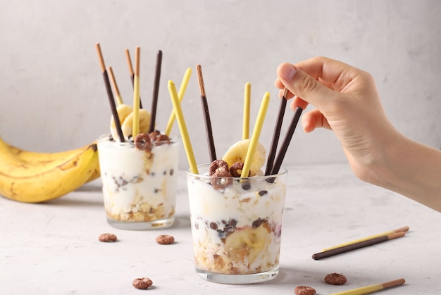 Due bicchieri di muesli con cioccolato e banana, decorata con bastoncini Pocky su sfondo grigio, primo piano