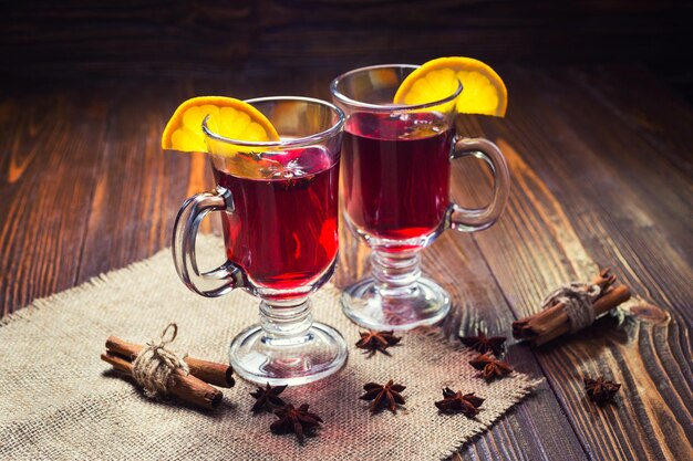 Due bicchieri di riscaldamento invernale bevanda calda rossa Natale vin brulé su sfondo di legno con fette di arancia speziata e bastoncini di cannella