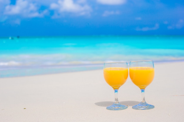 Due bicchieri di succo d'arancia sulla spiaggia bianca tropicale