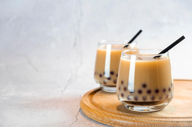 Due bicchieri di tè a bolle di latte con deliziose perle di tapioca su tavola di legno. Famoso tè alla gelatina di latte di Taiwan. Bevande gustose con copia spazio.