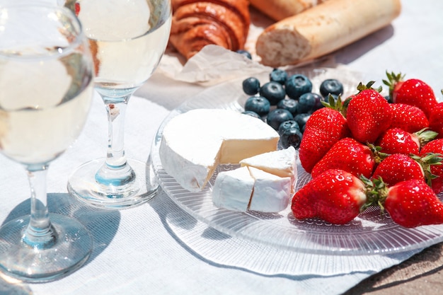 Due bicchieri di vino bianco e frutti di bosco, pasticcini, pane e formaggio camembert sul tavolo bianco allestito