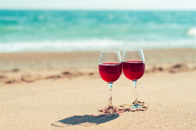 Due bicchieri di vino con vino rosso sulla sabbia della spiaggia in riva al mare Coppia romantica