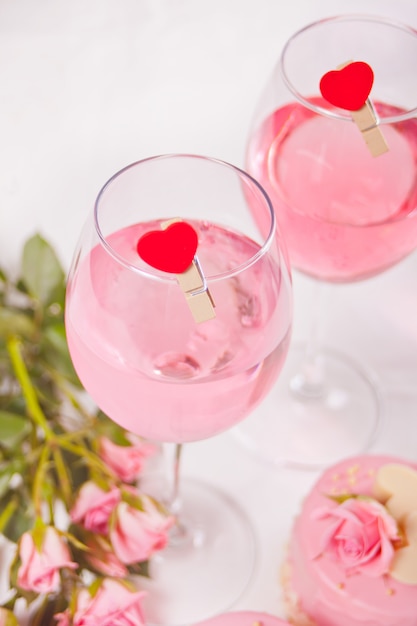 Due bicchieri di vino d'uva rosa con molletta a forma di cuore e rose. Concetto di cena romantica.