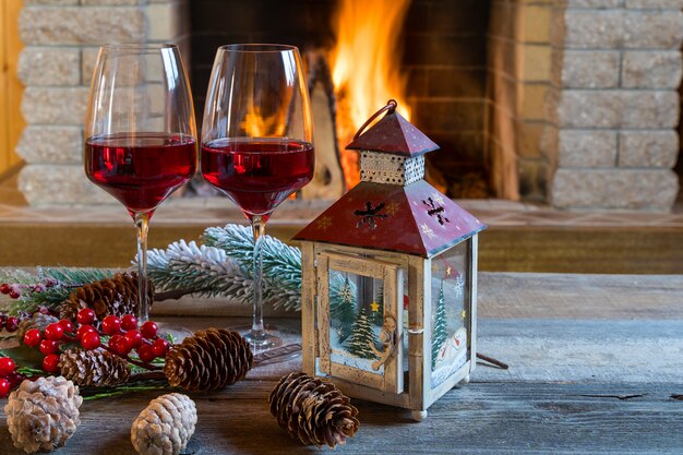 Due bicchieri di vino e lanterna di natale vicino al camino accogliente, in casa di campagna.