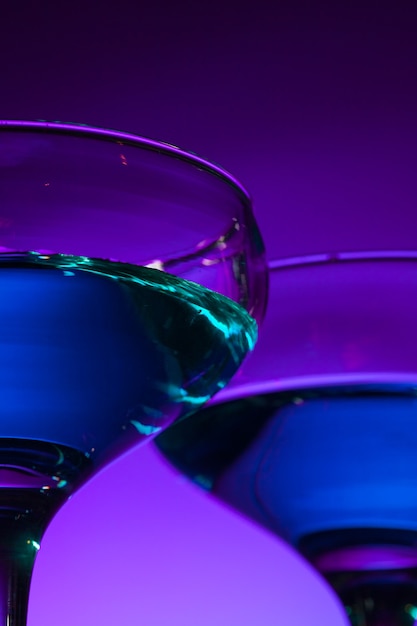 Due bicchieri di vino ripieni in piedi sul tavolo in studio. Illuminazione dai colori vivaci e luminosi. Trendy nel 2018 Lampadina Ultra Violetta. Decorazione d'arte con tono di colore mistico