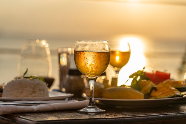 Due bicchieri di vino sul tavolo di legno vicino al mare sulla spiaggia tropicale durante il tramonto