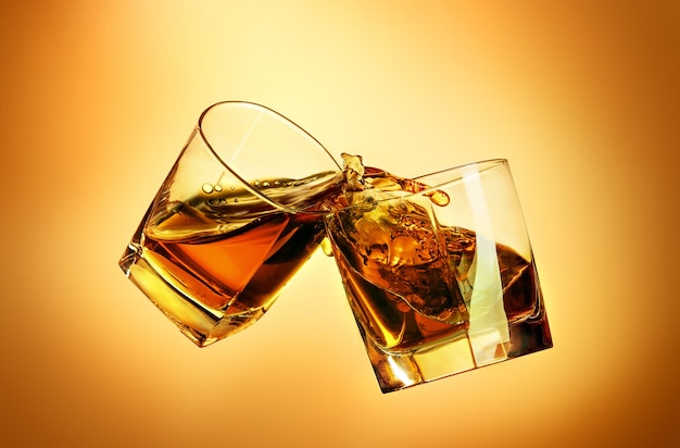 Due bicchieri di whisky che tintinnano insieme sullo sfondo marrone dello studio