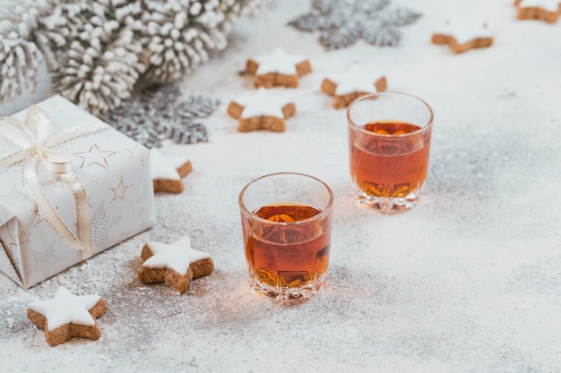 Due bicchieri di whisky o bourbon, biscotti a stella e decorazioni su sfondo bianco. Concetto di umore del whisky invernale