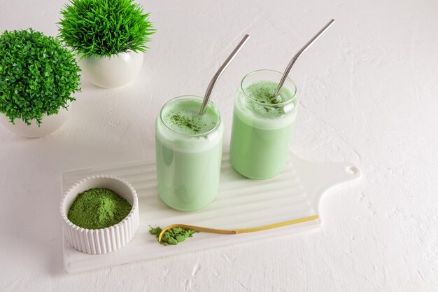 Due bicchieri moderni a forma di lattina di birra con tè verde matcha latte su una lavagna bianca con una ciotola di bevanda biologica naturale in polvere di matcha verde