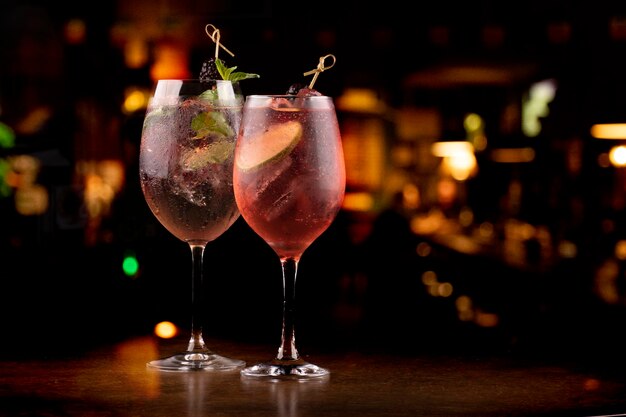 Due bicchieri rinfrescanti di lillet spritz aperol cocktail con bacche di lime e menta e ghiaccio su tavolo di legno con sfondo pub sfocato visto dalla parte anteriore