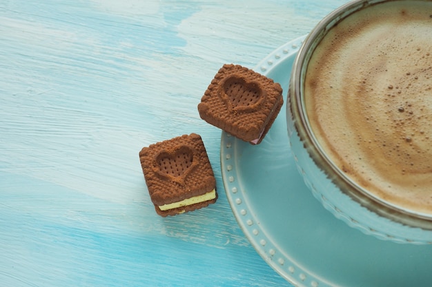 Due biscotti a forma di cuore su un piattino vicino a una tazza di caffè.