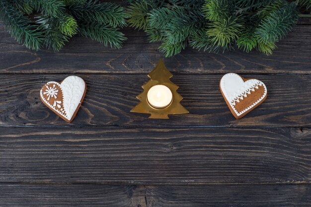 due biscotti di pan di zenzero a forma di cuore, un candeliere a forma di albero di Natale e rami di pino