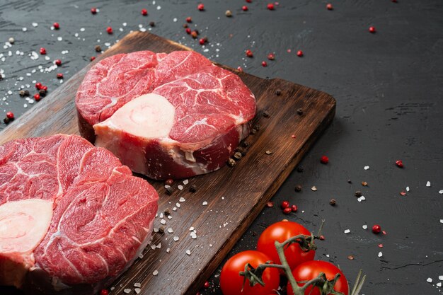 Due bistecca di carne marmorizzata fresca cruda su sfondo scuro, pomodorini e spezie. Avvicinamento.