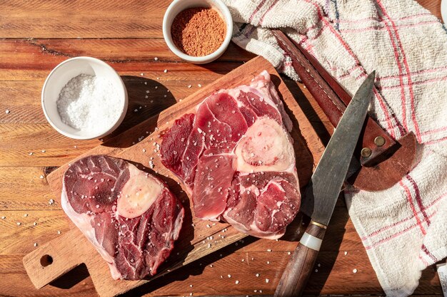 Due bistecche di ossobuco di manzo crudo su una tavola di legno con condimento per insaporire i pezzi di carne Concetto di proteine animali tagli economici di manzo Vista aerea