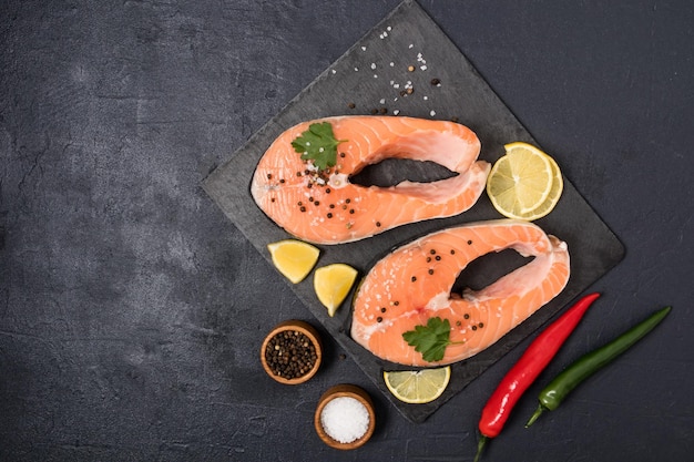 Due bistecche di salmone crudo su una tavola di pietra con pepe nero sale fette di limone fonte di omega 3 e grassi insaturi vista dall'alto sfondo nero