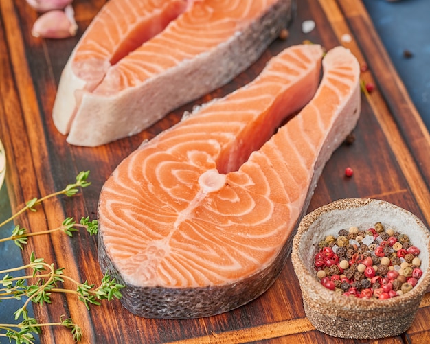 Due bistecche di salmone, filetto di pesce, grandi fette tagliate su un tagliere sul tavolo scuro