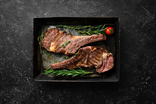 Due bistecche di vitello con osso con spezie, timo e rosmarino Carne al barbecue Vista dall'alto Vista dall'alto piatta su tavolo da taglio in pietra nera