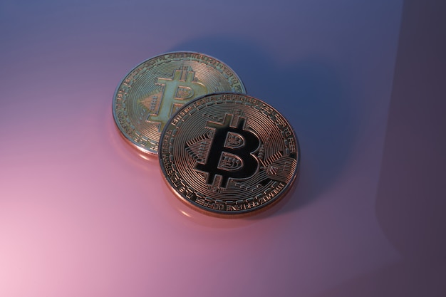 Due bitcoin dorati isolati sul primo piano porpora rosa del fondo con lo spazio della copia