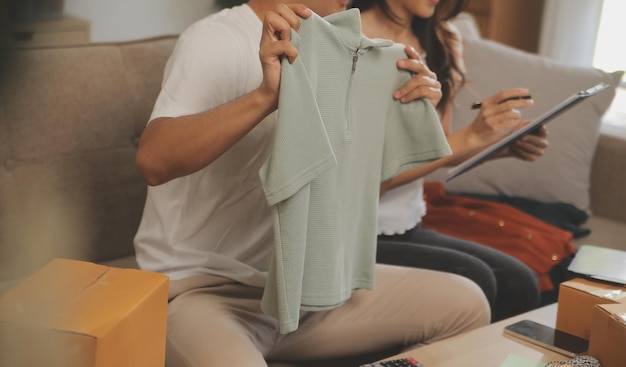 Due blogger asiatiche che mostrano vestiti davanti alla telecamera per registrare video vlog in streaming live nel suo negozio Carrello della spesa online sul divano di casa