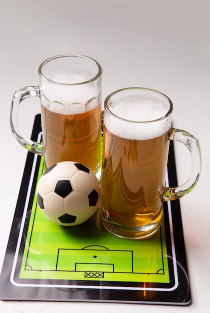 Due boccali di birra schiumosa, calcio balilla, palla sul tavolo bianco