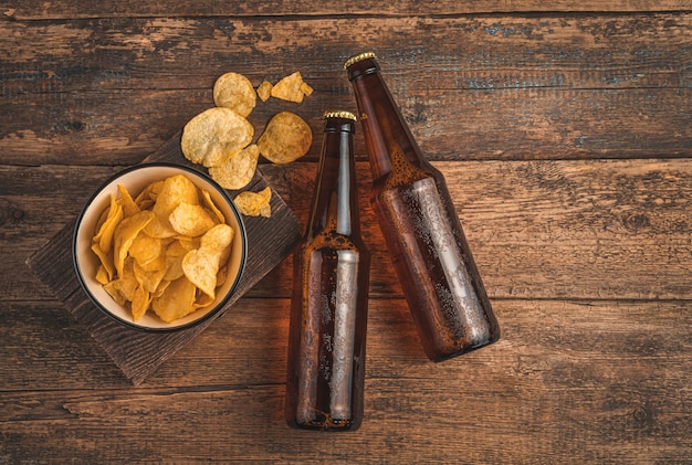 Due bottiglie di birra e patatine su uno sfondo di legno marrone. Vista dall'alto, copia dello spazio.