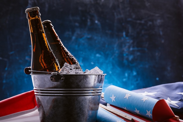 due bottiglie di birra in un secchiello del ghiaccio con la bandiera americana nelle vicinanze e i razzi per i fuochi d'artificio. Concetto di celebrazione della festa dell'indipendenza