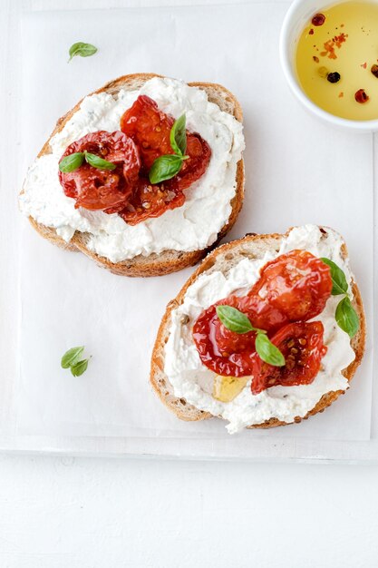 Due bruschette con ricotta, olive e pomodori secchi su ciabatta su fondo bianco