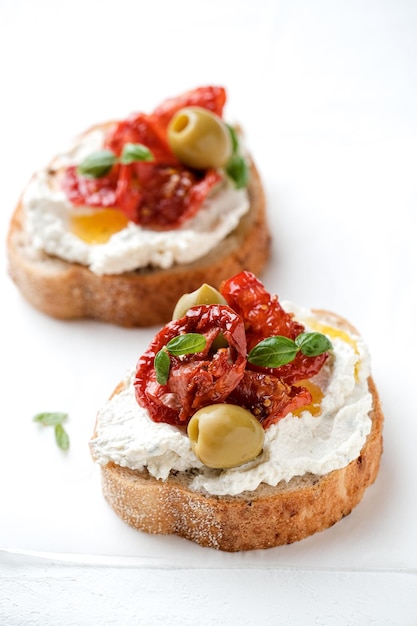 Due bruschette con ricotta, olive e pomodori secchi su ciabatta su fondo bianco