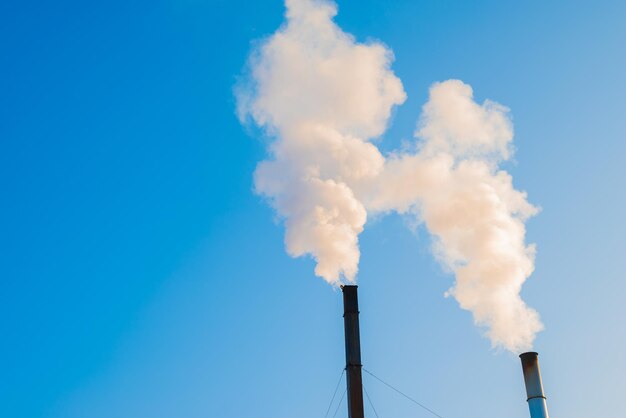 Due camini di fabbrica fumanti contro un cielo blu. Aumentare le emissioni di CO2 e di gas serra.