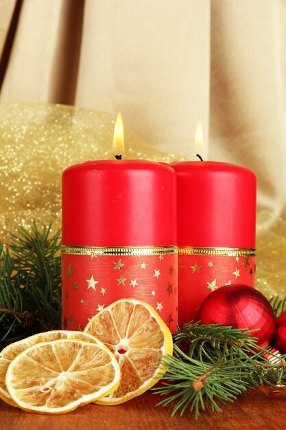 Due candele e decorazioni natalizie, su sfondo di stoffa dorata