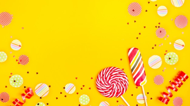 Due caramelle multicolori tra cerchi di carta di confetti, glitter e nastri festosi