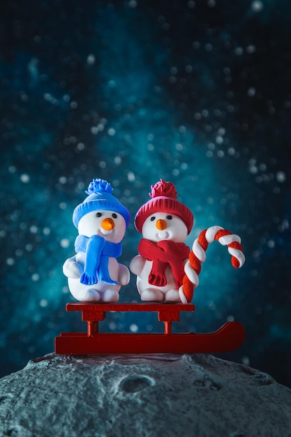 Due carini uomini di neve di plasticina con una slitta e un lecca-lecca sulla luna carta di Natale