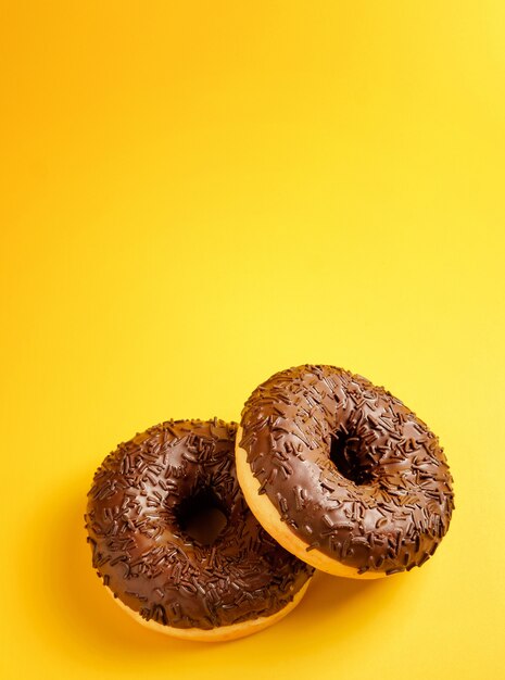 Due ciambelle al cioccolato su sfondo giallo vista dall'alto