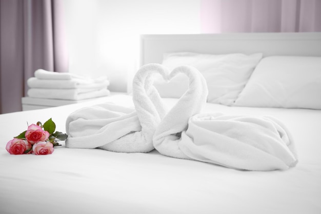 Due cigni asciugamano e bouquet di rose sul letto nella camera d'albergo