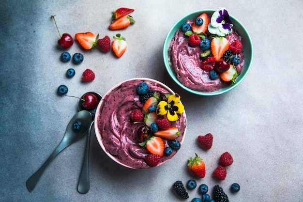 Due ciotole di frullato di acai estivo con fragole mirtilli su sfondo grigio cemento Ciotola colazione con frutta e cereali primo piano vista dall'alto cibo sano