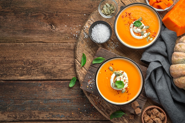 Due ciotole di zuppa di crema di zucca con crema di basilico e semi di zucca su fondo marrone