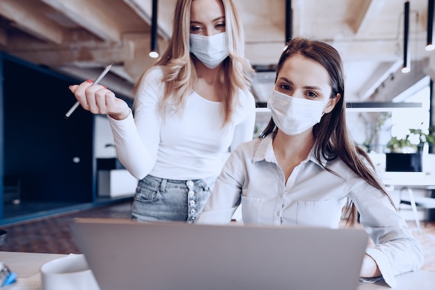 Due colleghe che lavorano insieme in ufficio indossando maschere mediche