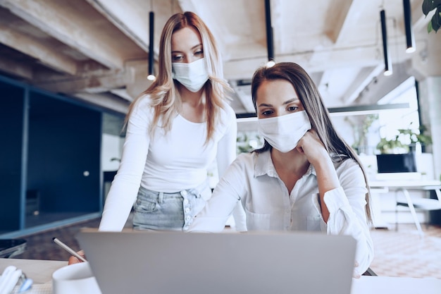 Due colleghe che lavorano insieme in ufficio indossando maschere mediche