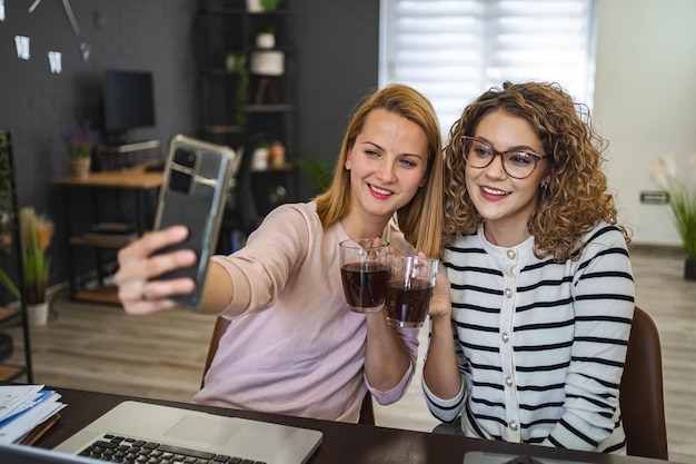 Due colleghe stanno facendo dei selfie e bevendo caffè.