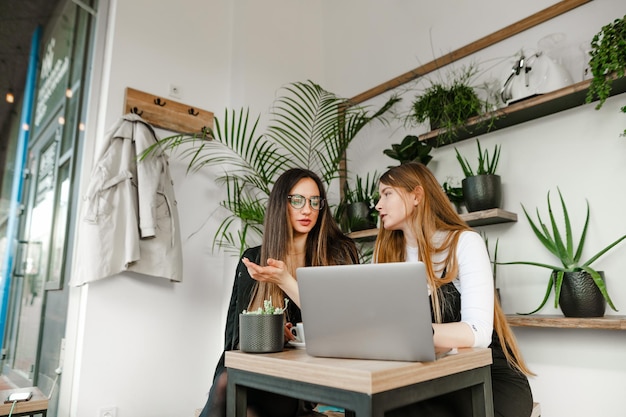 Due colleghi di donne d'affari seduti in un caffè portatile elegante e luminoso che discutono di lavoro con facce serie