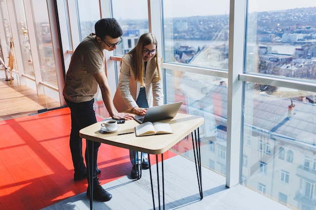 Due colleghi, un uomo e una donna manager, stanno vicino a un tavolo con un laptop in un ufficio moderno e discutono di un nuovo progetto Due soci in affari con gli occhiali stanno parlando di una nuova attività