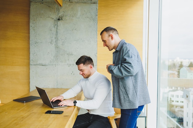 Due colleghi uomini lavorano con un laptop in ufficio Due imprenditori orientati all'obiettivo collaborano in uno spazio di lavoro moderno Due giovani uomini d'affari lavorano in un ufficio luminoso