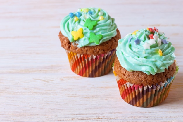 Due coloratissimi cupcakes fatti a mano con crema verde su uno sfondo di legno bianco.