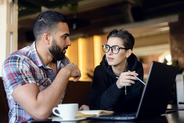 Due compagni di classe intelligenti che hanno una conversazione amichevole mentre fanno i compiti con il laptop all'interno del bar